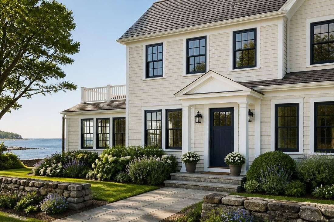Classic New England coastal home with warm ivory siding, black trim, and a navy blue front door